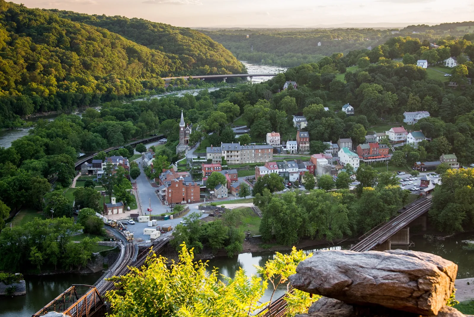 Harpers Ferry's historic riverside buildings surrounded by green hills, viewed from Maryland Heights.
